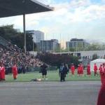 Two groups of graduates in cap and gown line up at Memorial Stadium